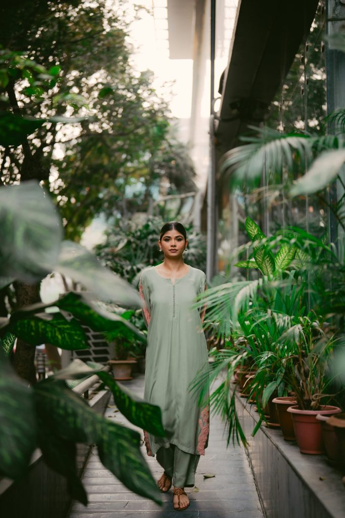 Woman walks through a lush, green greenhouse.